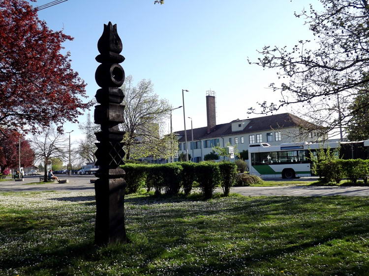A Rockenbauer Pál kopjafa a buszállomás kis parkjában áll. Háttérben a vasútállomás épülete látható.