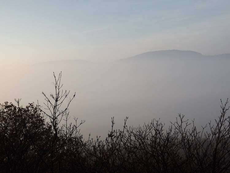 Kilátás a ködből kiemelkedő Hármashatár-hegyre és Csúcs-hegyre a Köves-bércről